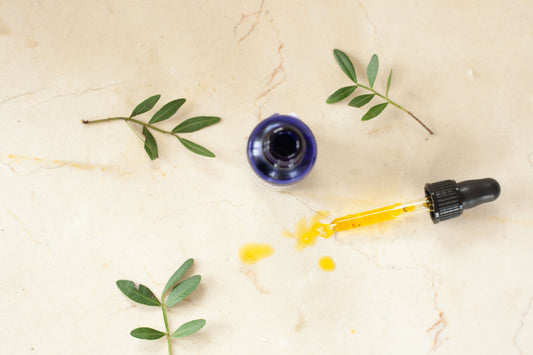 Overhead view of open facial serum bottle with glass dropper and golden oil on marble.