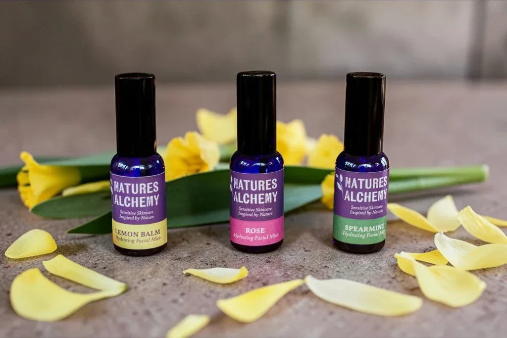 Three Natures Alchemy hydrating facial mists in Lemon Balm, Rose and Spearmint with yellow daffodils on a stone surface