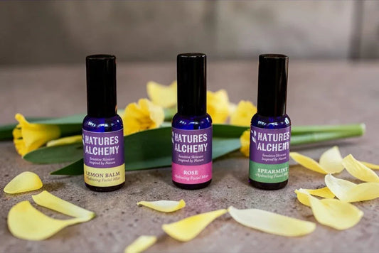 Three Natures Alchemy hydrating facial mists in Lemon Balm, Rose and Spearmint with yellow daffodils on a stone surface