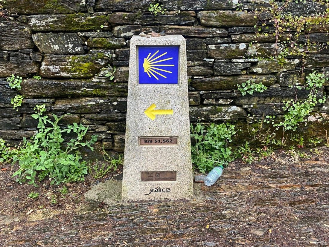 Camino de Santiago waymarker km 51 - pilgrimage route marker with yellow arrow and scallop shell symbol Spain