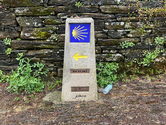 Camino de Santiago waymarker km 51 - pilgrimage route marker with yellow arrow and scallop shell symbol Spain