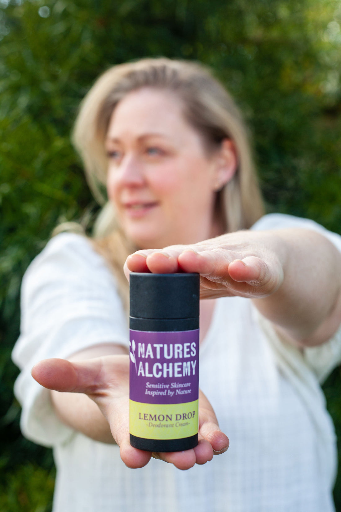 Lynn from Natures Alchemy holding a Lemon Drop natural deodorant cream in a garden setting in Ireland