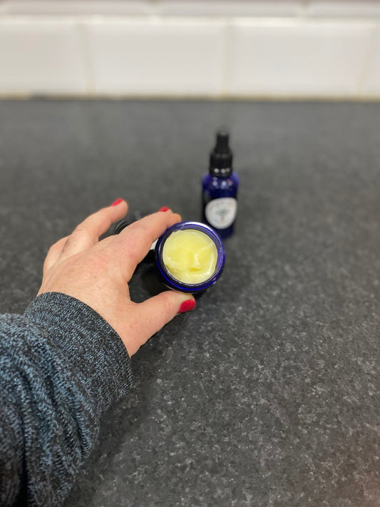 Hand holding a glass jar of Natures Alchemy whipped balm