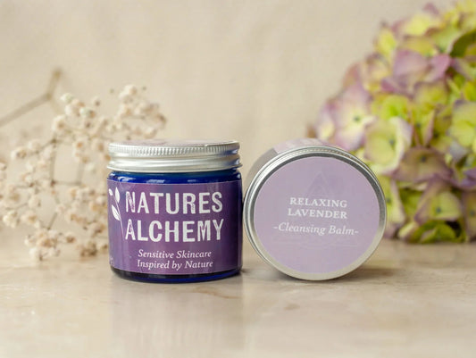 Natures Alchemy Relaxing Lavender Cleansing Balm jar with lid beside dried flowers and hydrangeas on a light wooden surface