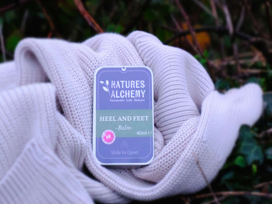 Heel & Feet Balm in reusable tin resting on soft knit fabric outdoors, natural herbal foot care by Natures Alchemy